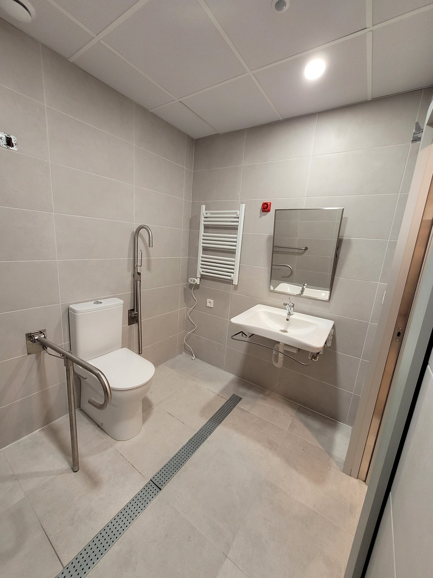 Aseo accesible con inodoro con barras abatibles, lavabo sin pedestal y sumidero lineal enrasado
