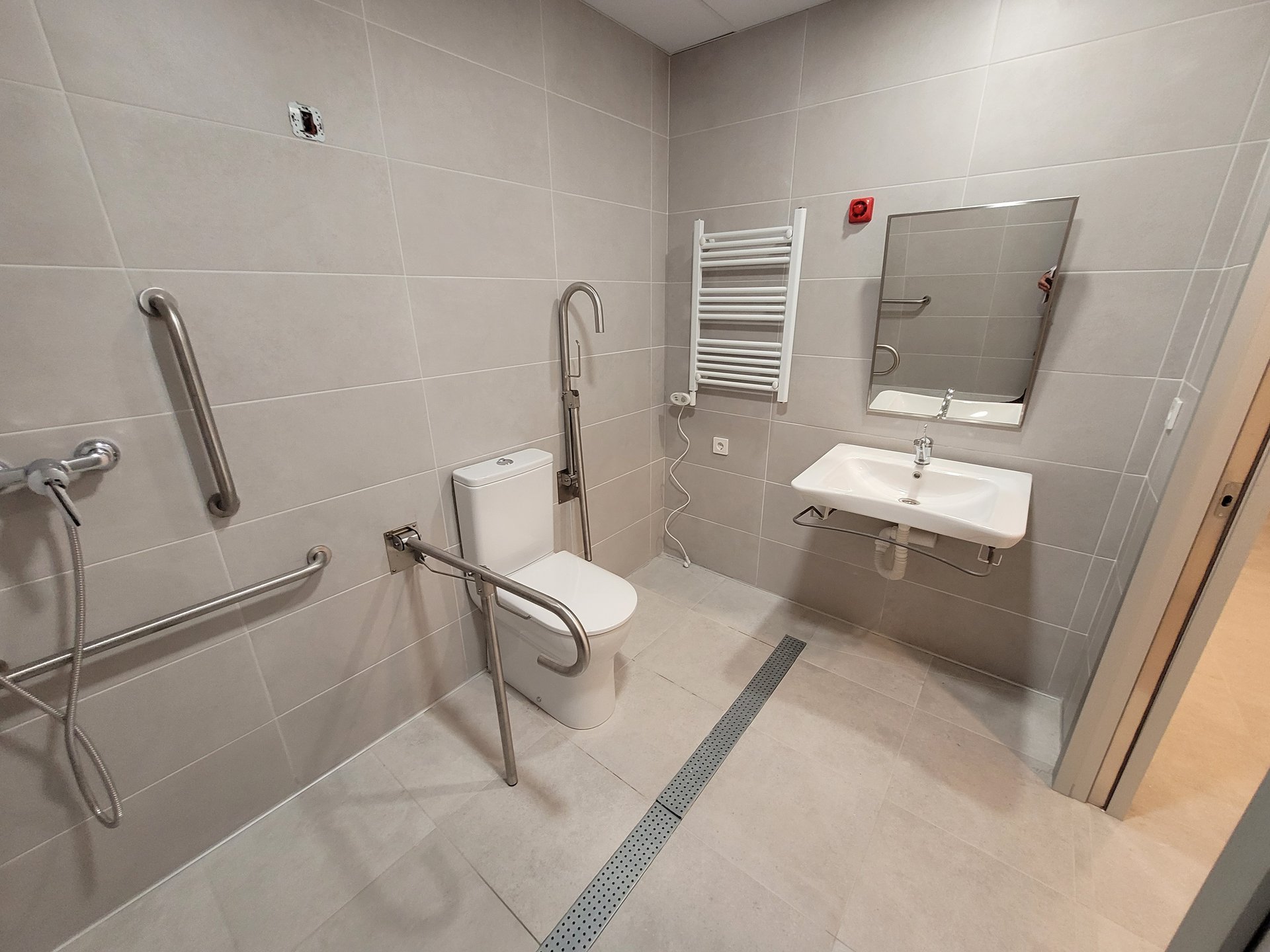 Baño accesible con barras de apoyo, ducha enrasada y lavabo sin pedestal