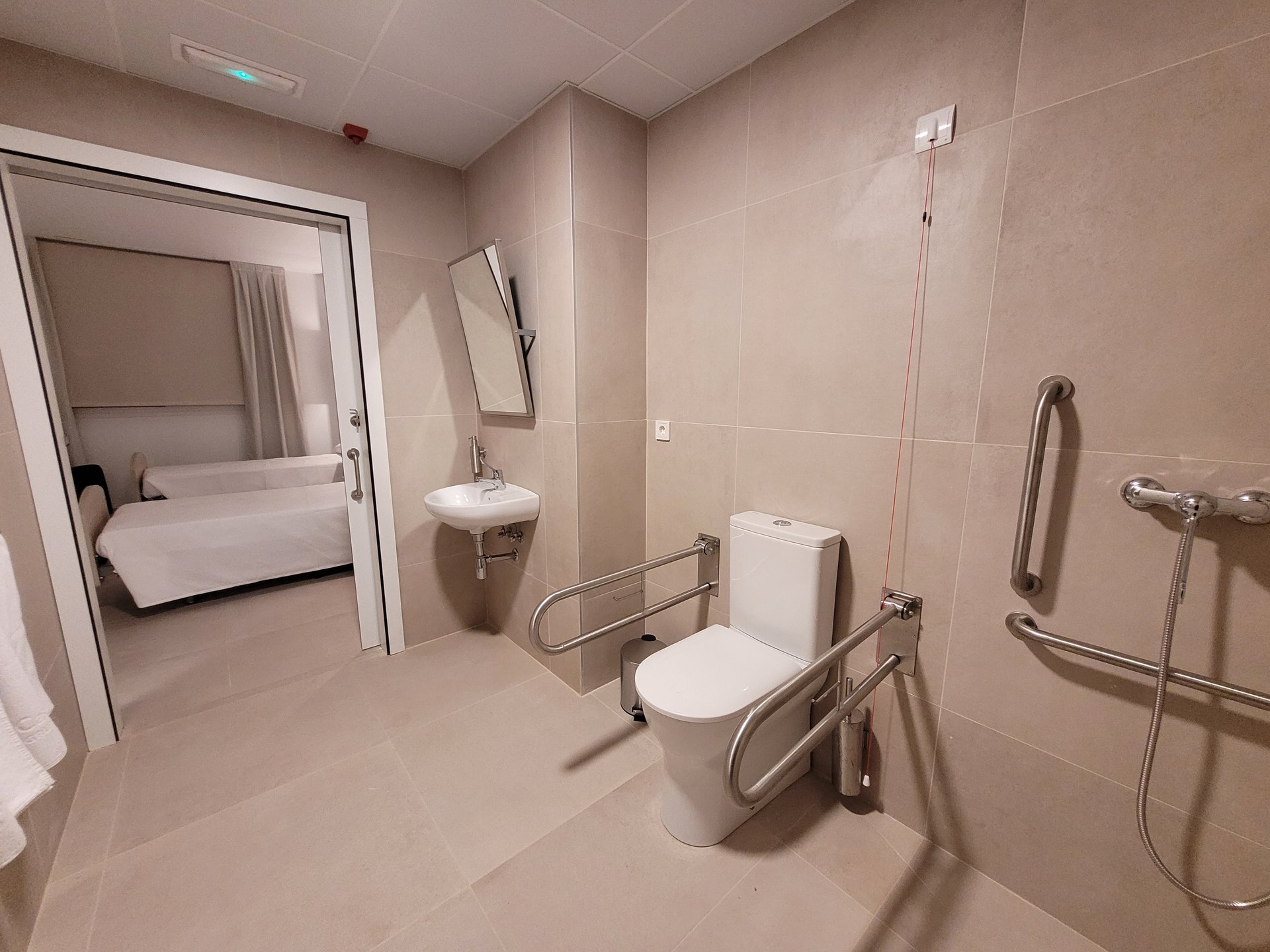 Baño adaptado de una habitación de hotel con barras de apoyo y acceso directo al dormitorio