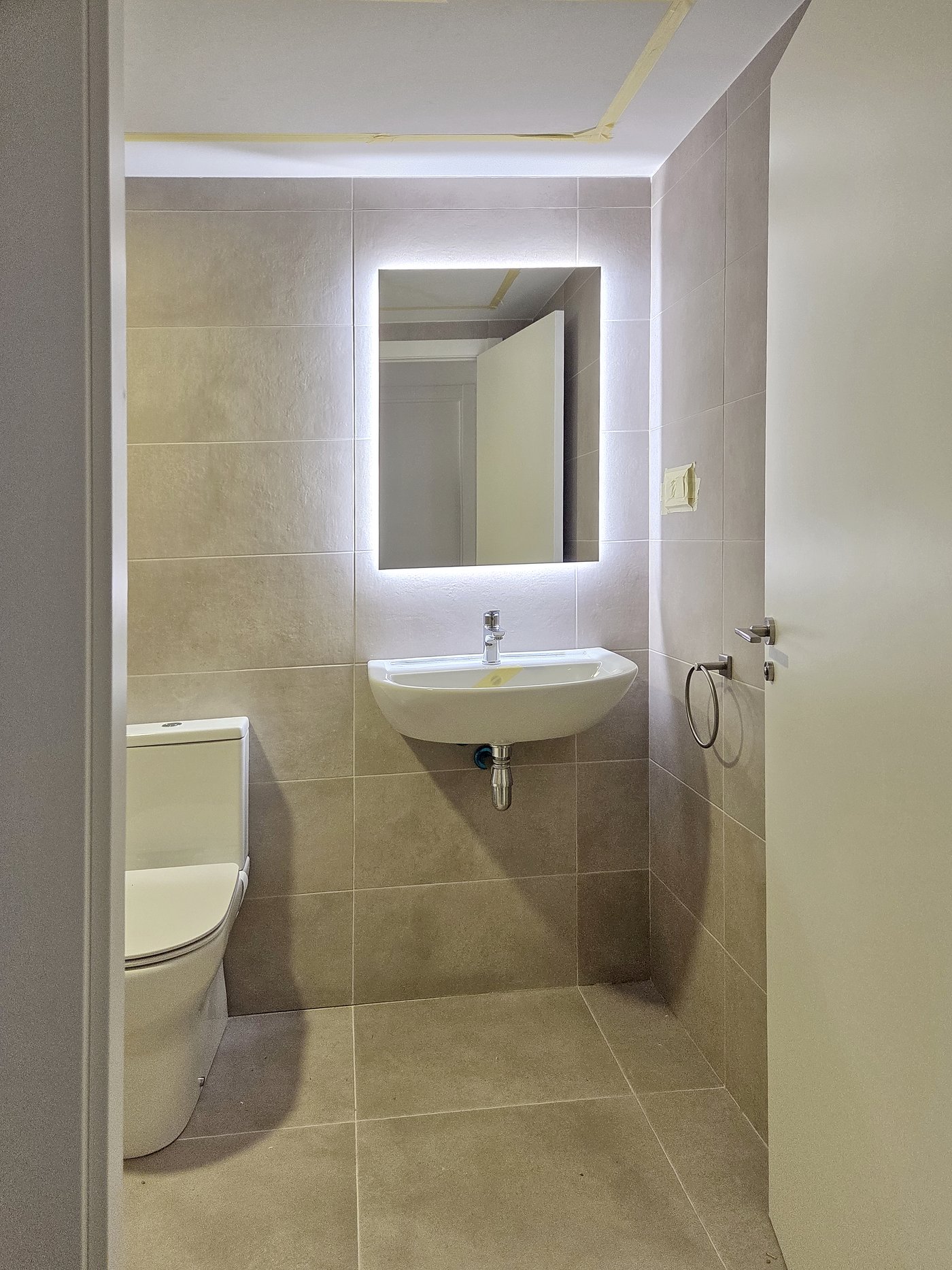 Baño industrializado terminado en una vivienda asequible, con lavabo, espejo retroiluminado e inodoro