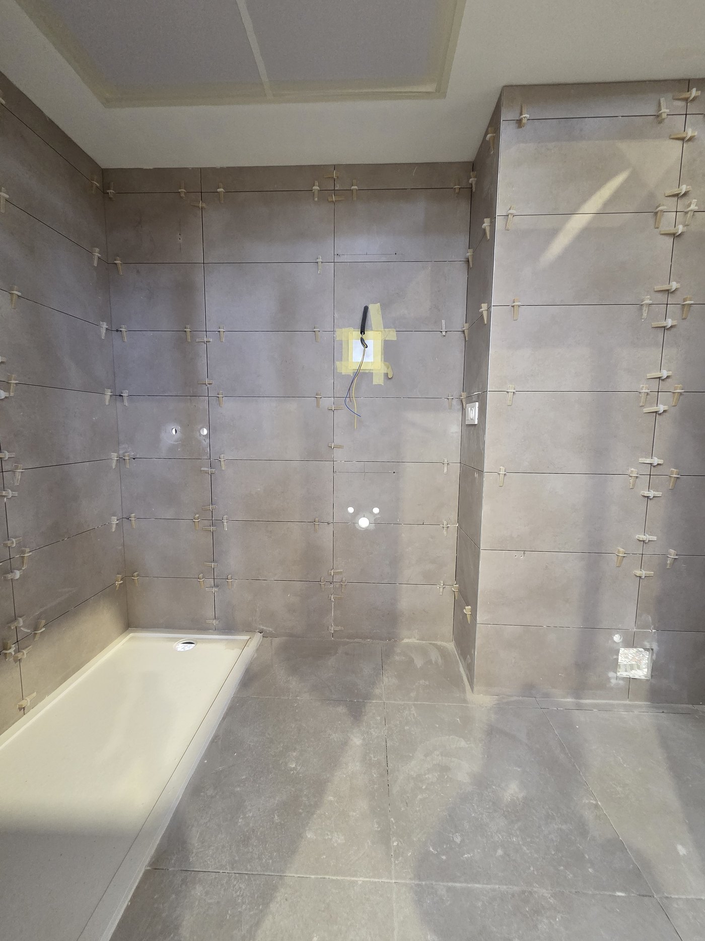 Revestimiento cerámico de gran formato con niveladores y plato de ducha en el interior de un baño industrializado
